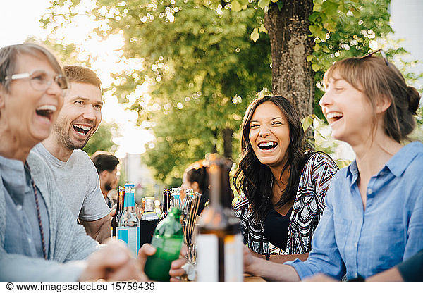 Male and female friends laughing while sitting with drinks at beer garden