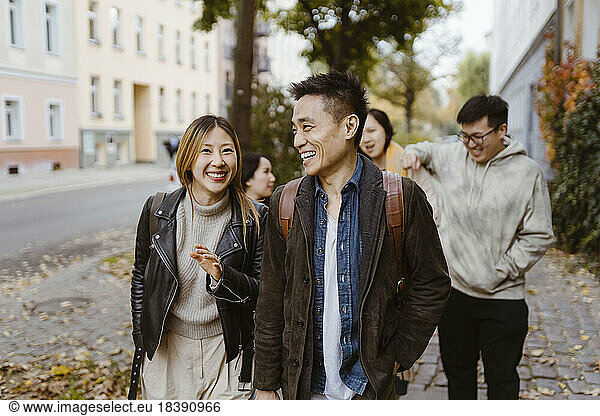 Male and female friends laughing while walking on sidewalk