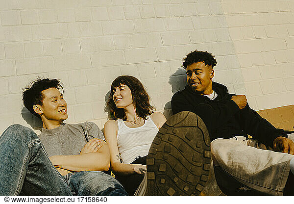 Male and female friends talking against wall during sunny day
