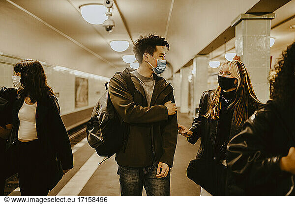 Male and female friends talking at illuminated subway station during COVID-19
