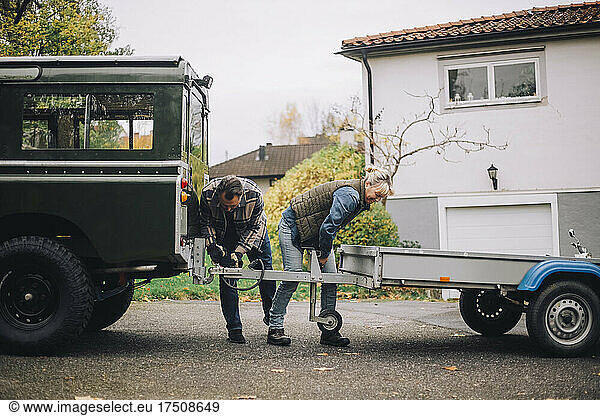 Male and female friends towing trailer to sports utility vehicle at driveway