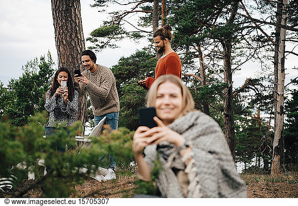 Male and female friends using smart phones while resting at forest