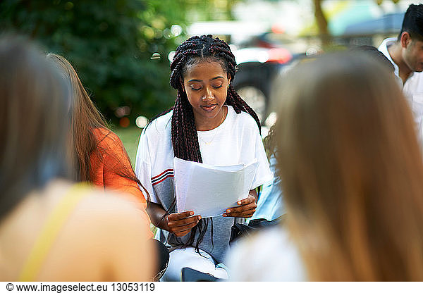 Male and female higher education student looking at paperwork on college campus lawn  over shoulder view