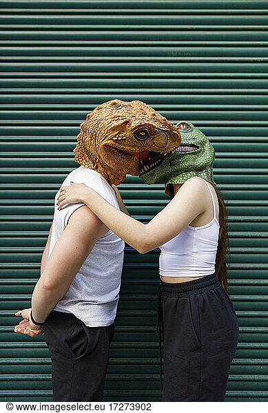 Male and female in dinosaur mask kissing against green shutter