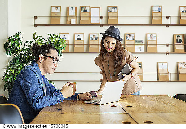 Male and female Japanese professional at a table in a co-working space  using laptop computer.