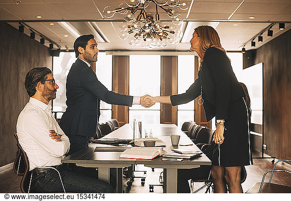 Male and female lawyers shaking hands in board room at office