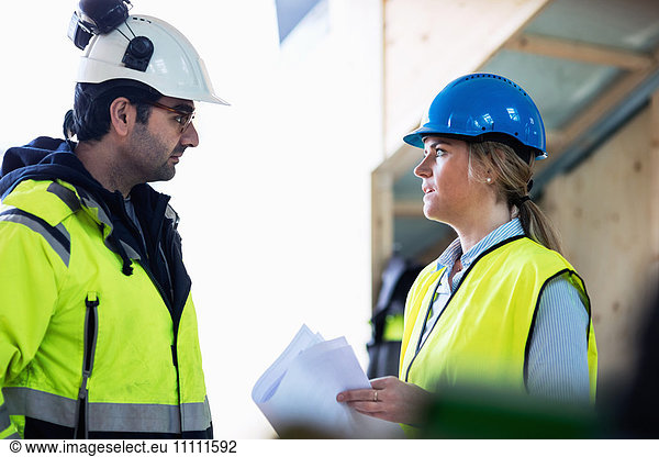 Male and female managers discussing over document at construction site