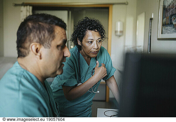 Male and female medical professionals discussing over computer in hospital