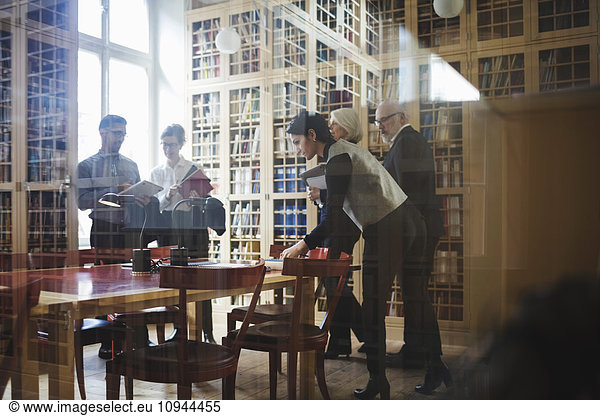 Male and female professionals standing in board room seen through glass