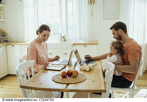 Male and female professionals working at dining table in kitchen