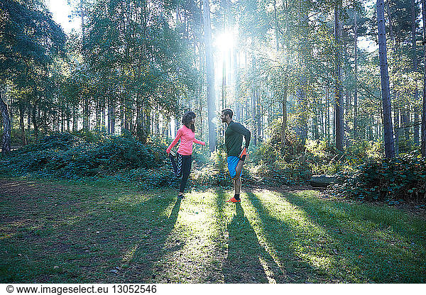 Male and female runners stretching legs and warming up in sunlit forest
