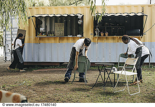 Male and female sellers arranging chairs and table by food truck in park