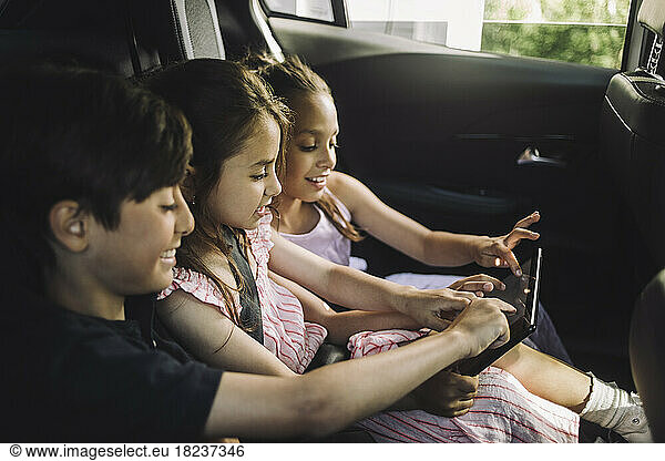 Male and female siblings using tablet PC while traveling in car