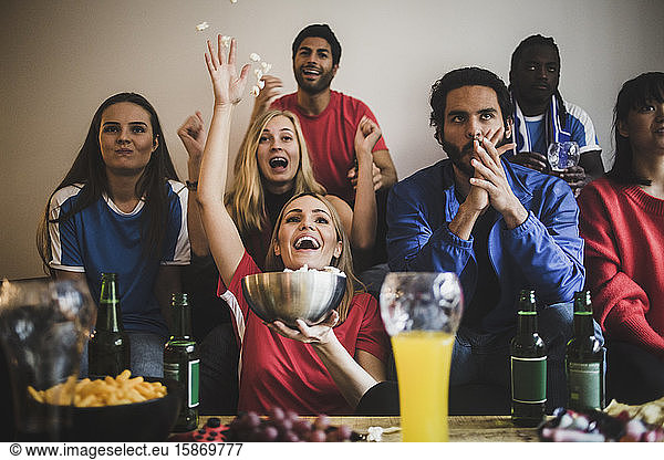 Male and female soccer fans watching match while sitting on sofa at home
