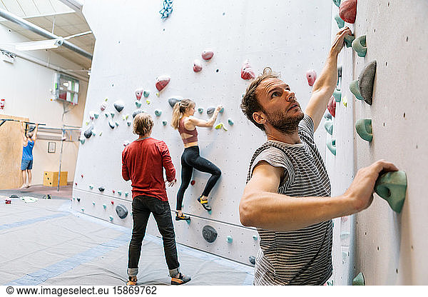 Male and female students practicing wall climbing while mature coach training in gym
