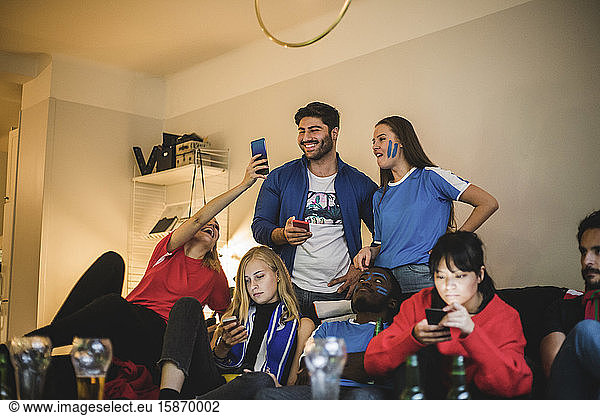 Male and female using smart phone while watching soccer match at home