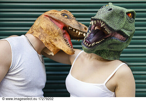 Male and female wearing dinosaur mask against green metallic shutter