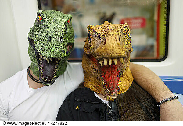 Male and female wearing dinosaur mask while traveling in train