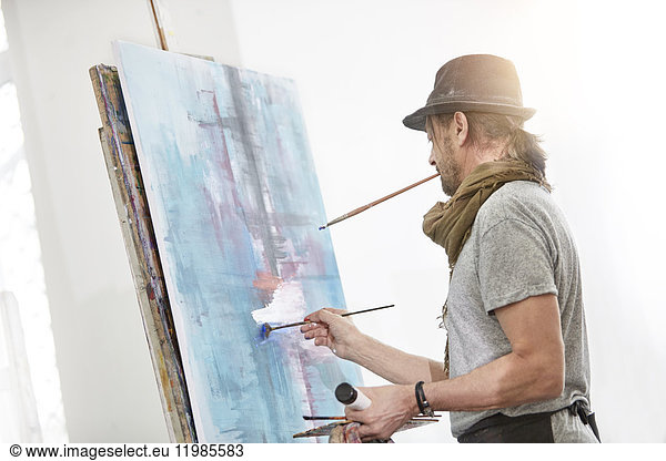 Male artist painting at easel in art studio
