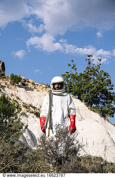 Male astronaut wearing space suit standing on mountain against sky