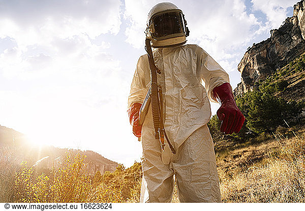 Male astronaut wearing space suit standing on mountain against sky during sunny day