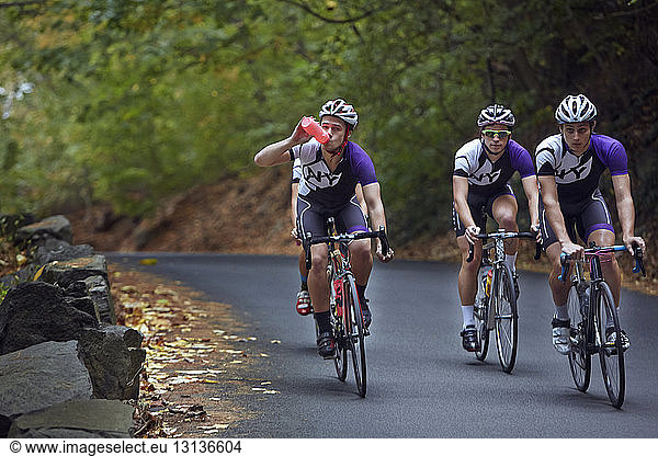 Male athlete drinking water while riding bicycle with friends
