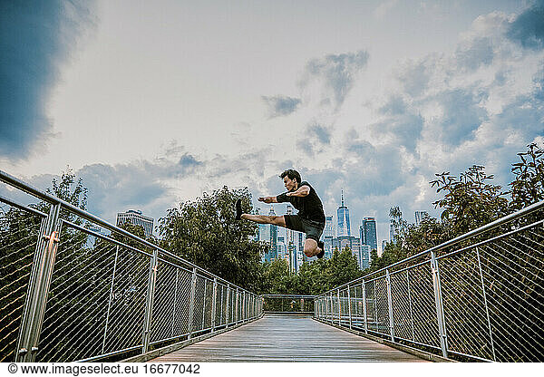 Male athlete jumping mid air in city park during sunset.