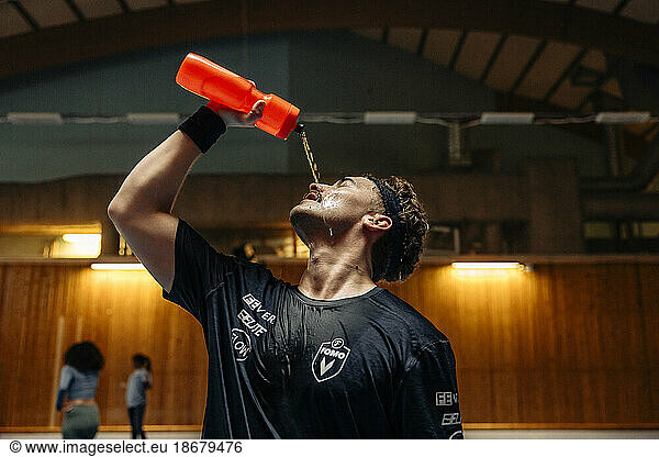 Male athlete pouring water on face from bottle at sports court