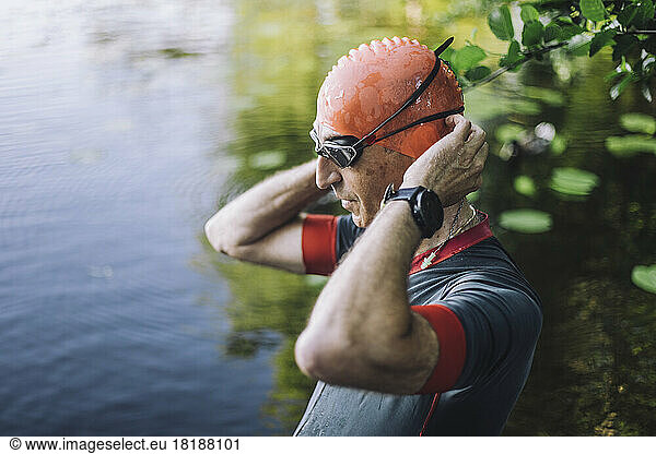 Male athlete preparing for swim while adjusting swimming cap in lake