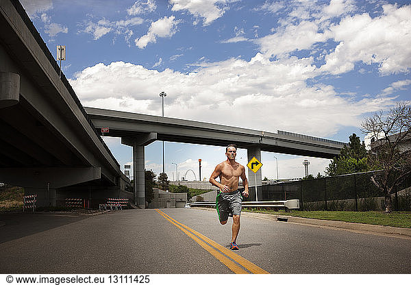 Male athlete running on road against cloudy sky