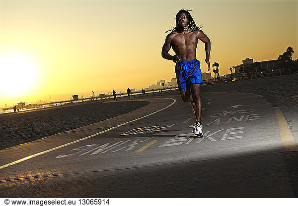 Male athlete running on road at sunset