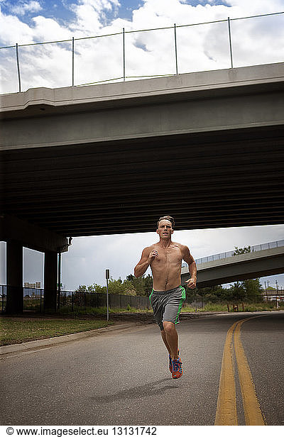 Male athlete running on road under bridge