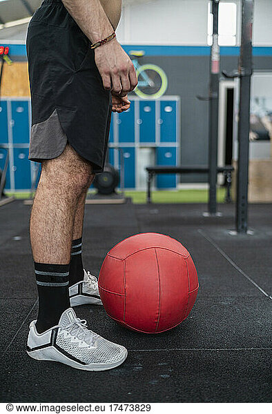 Male athlete standing by red sports ball in health club