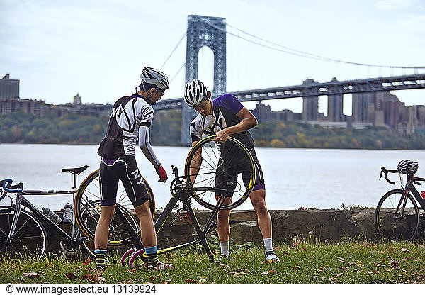 Male athletes repairing bicycle against George Washington Bridge
