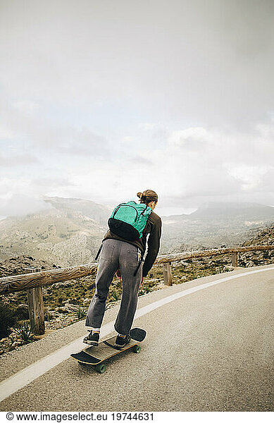 Male backpacker skateboarding on road against sky