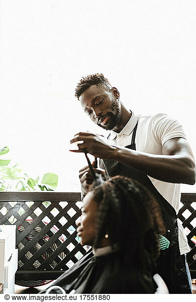 Male barber cutting hair of female customer in hair salon