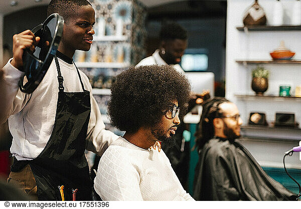 Male barber showing mirror to customer in hair salon