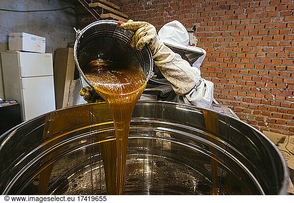 Male beekeeper pouring honey in storage tank