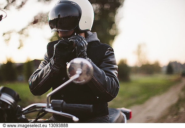 Male biker adjusting helmet while sitting on motorcycle