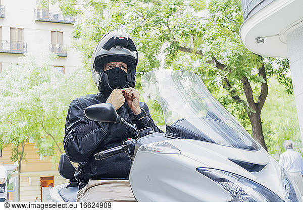 Male biker putting on helmet while sitting on motor scooter