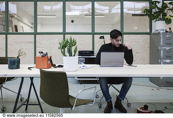 Male blogger sitting with laptop at desk in office