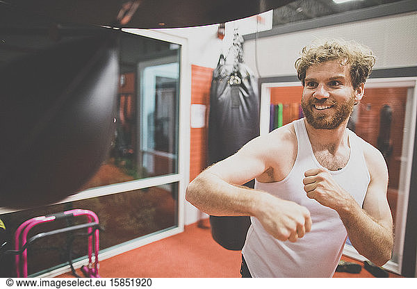 Male boxer happily uses punching bag at the gym