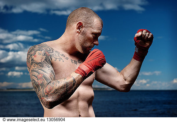 Male boxer practicing by sea against cloudy sky
