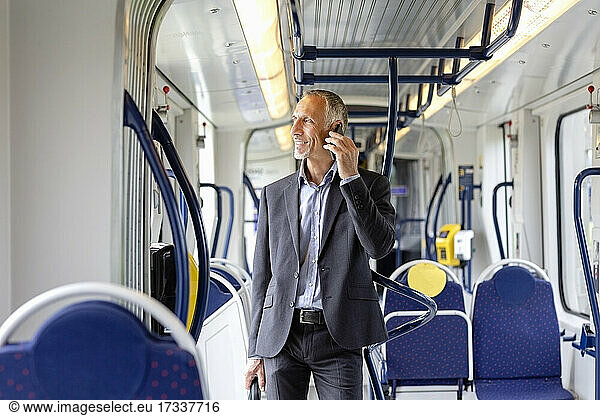 Male business professional looking away while talking on smart phone in tram