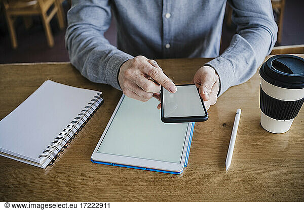 Male businessperson working on mobile phone and digital tablet at work place