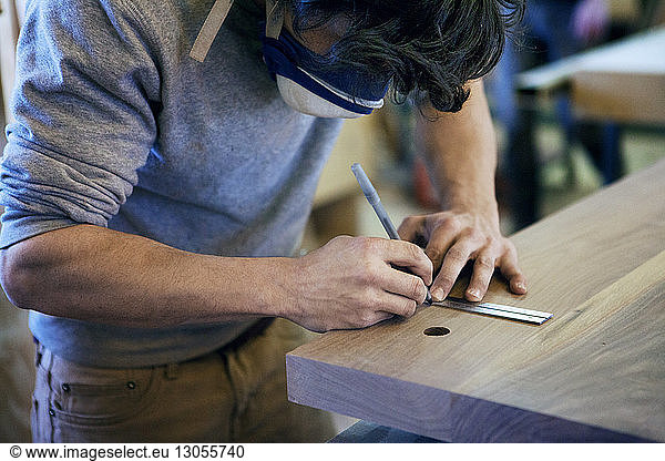 Male carpenter marking on wooden plank at workshop