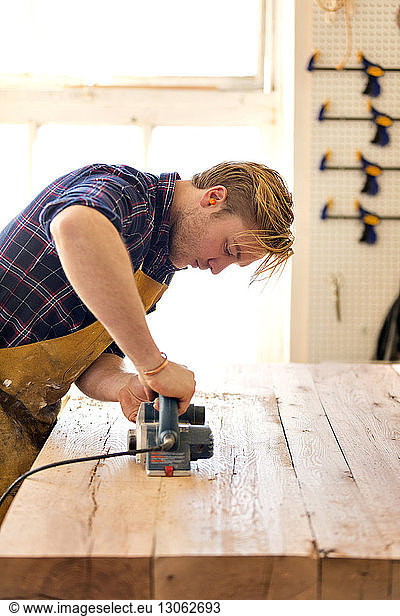 Male carpenter using equipment to cut wood in workshop