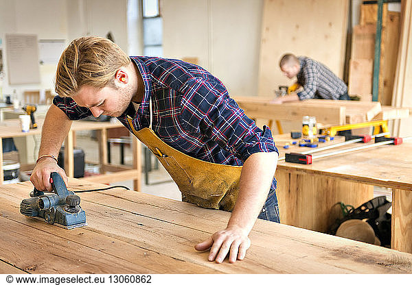 Male carpenter using tool to cut wood in workshop