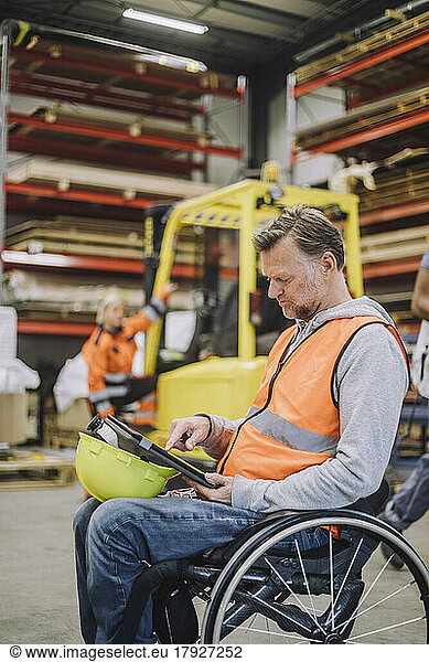 Male carpenter with disability using digital tablet sitting on wheelchair in warehouse