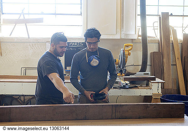 Male carpenters discussing over wooden plank at workshop